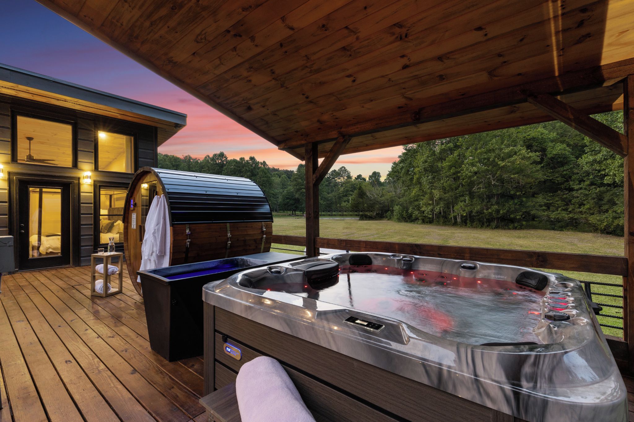 A hot tub on a wooden deck with a covered area, a barbecue grill, and a view of a forested area.