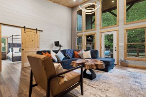 A modern living room with a leather chair, a blue sofa, and a wooden coffee table. - Private Creekfront Luxury: Sauna · Cold Plunge · Hot Tub · Fire pit · 4-acres (Mineral Bluff)