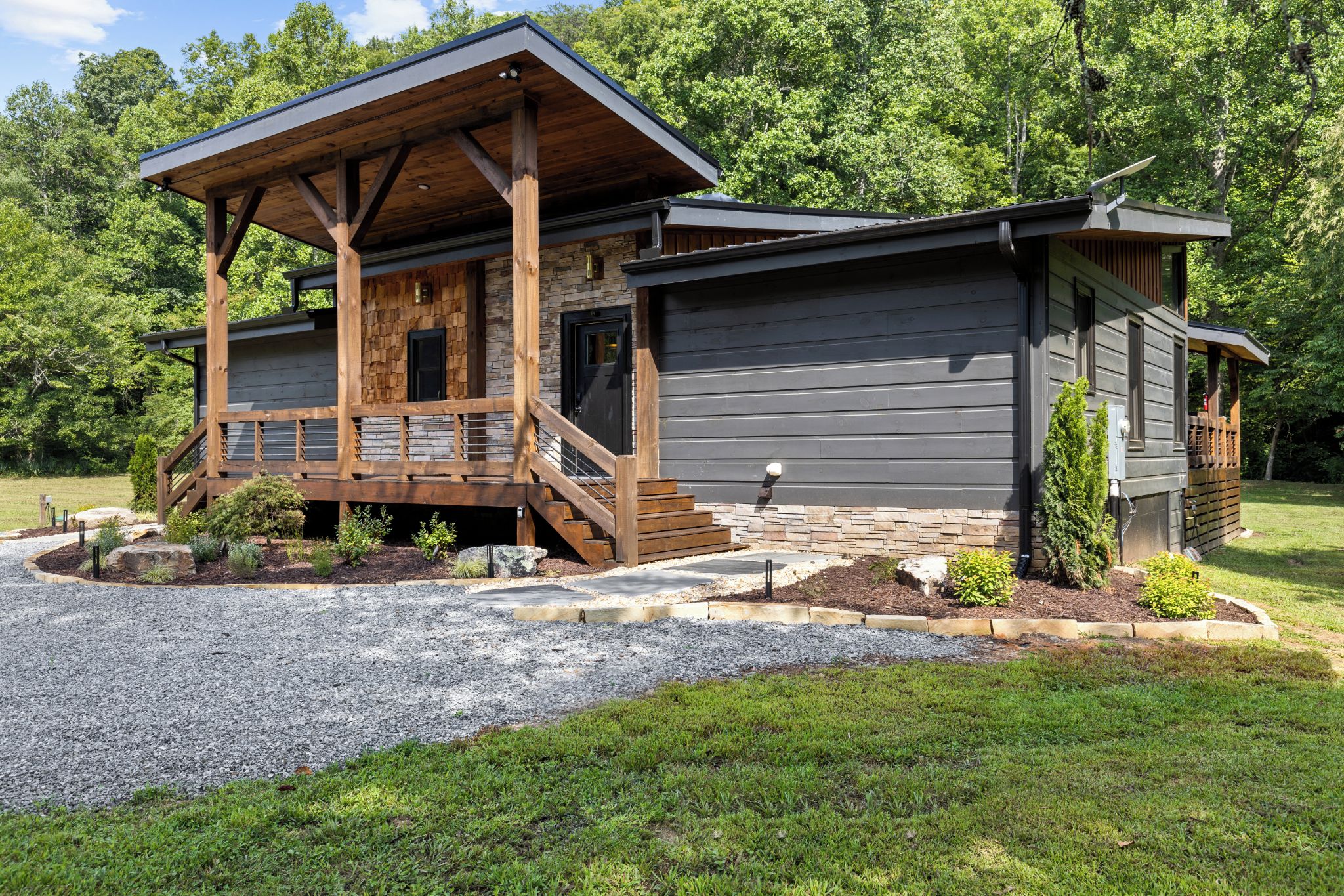 A cabin with a wooden deck, stone foundation, and a gravel driveway.