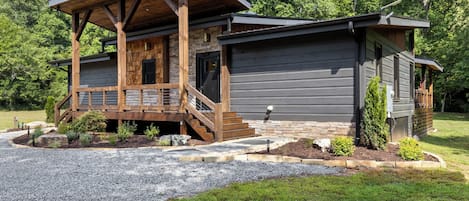 A cabin with a wooden deck, stone foundation, and a gravel driveway.