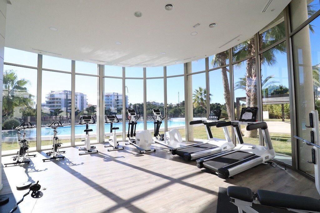 A gym with various exercise equipment, large windows, and a view of a swimming pool.