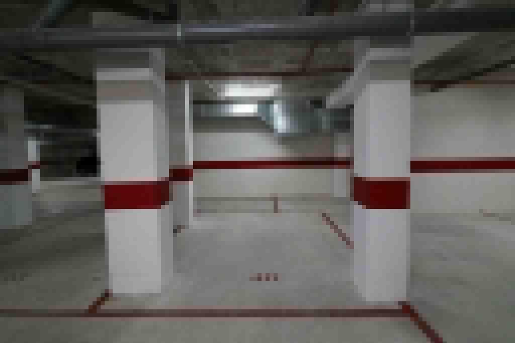 Un pasillo con pilares blancos y detalles en rojo, que conduce a una puerta.