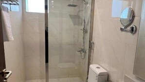 A modern bathroom with a glass-enclosed shower, a toilet, and a sink with a mirror. - Eioraa Hotel (Tara)