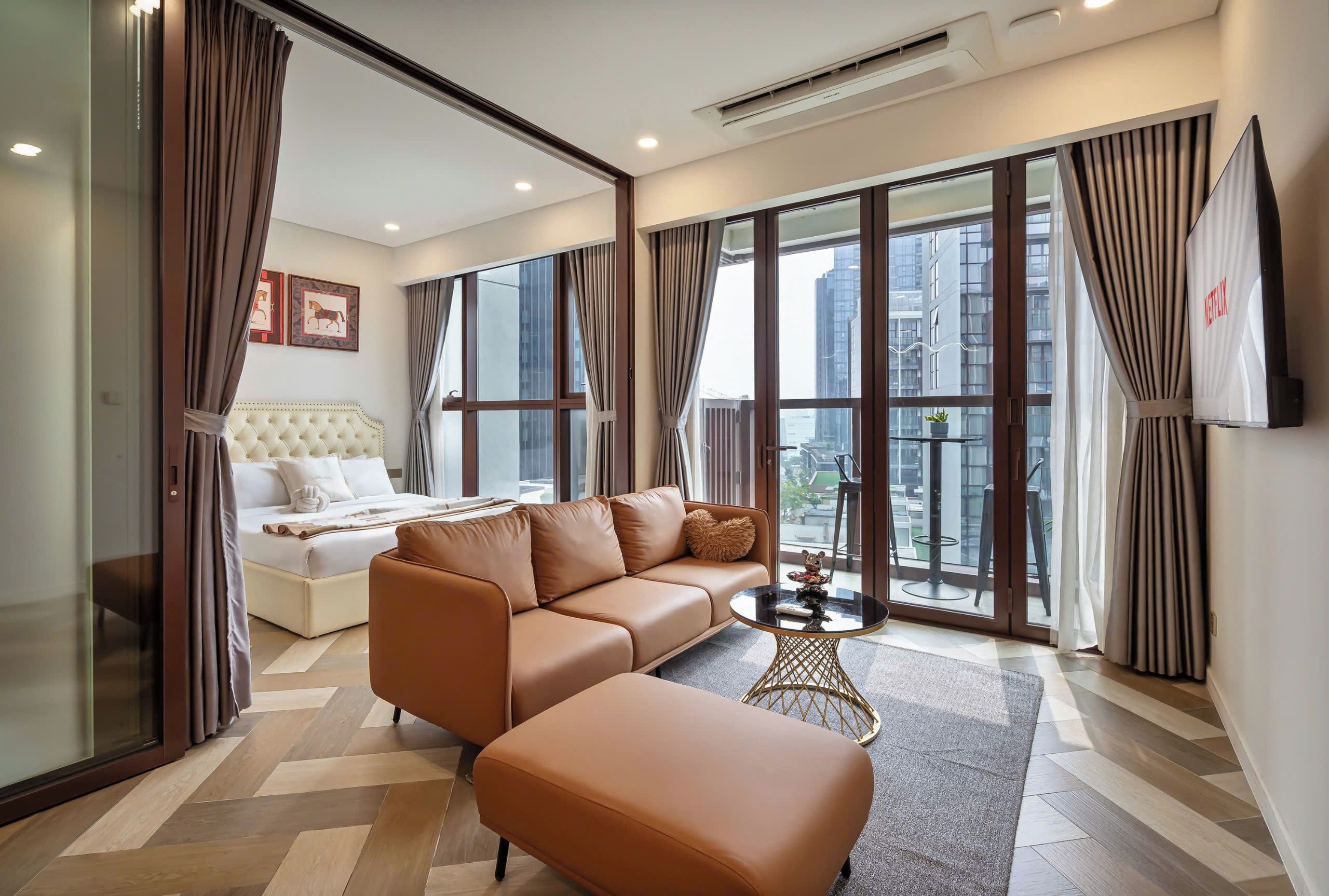 A modern hotel room with a sofa, ottoman, and a small table with decorative items.