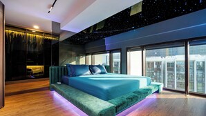 Un dormitorio moderno con una cama grande, un espacio de descanso y vistas a la ciudad.