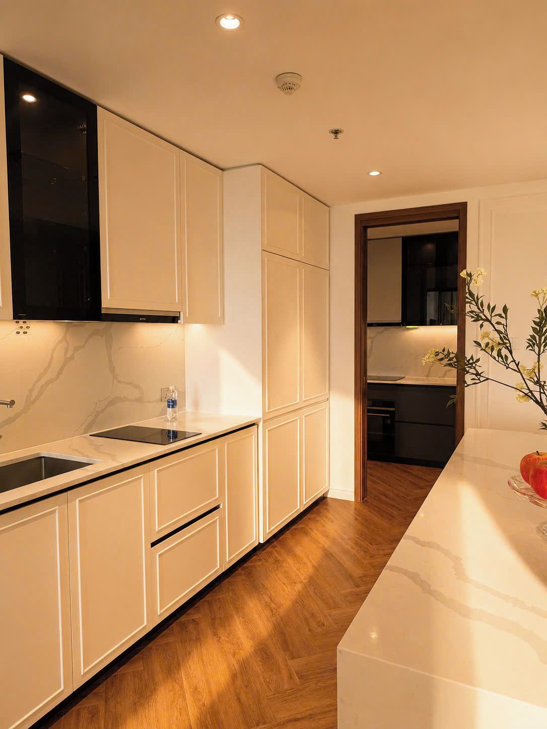 Una cocina moderna con muebles blancos, encimera de mármol y suelo de madera.