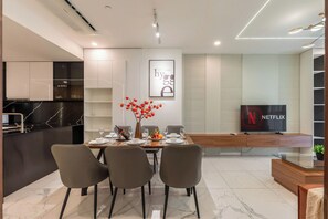 Un comedor moderno con una mesa preparada para cuatro, un televisor mostrando el logotipo de Netflix, y una cocina con encimera de mármol.