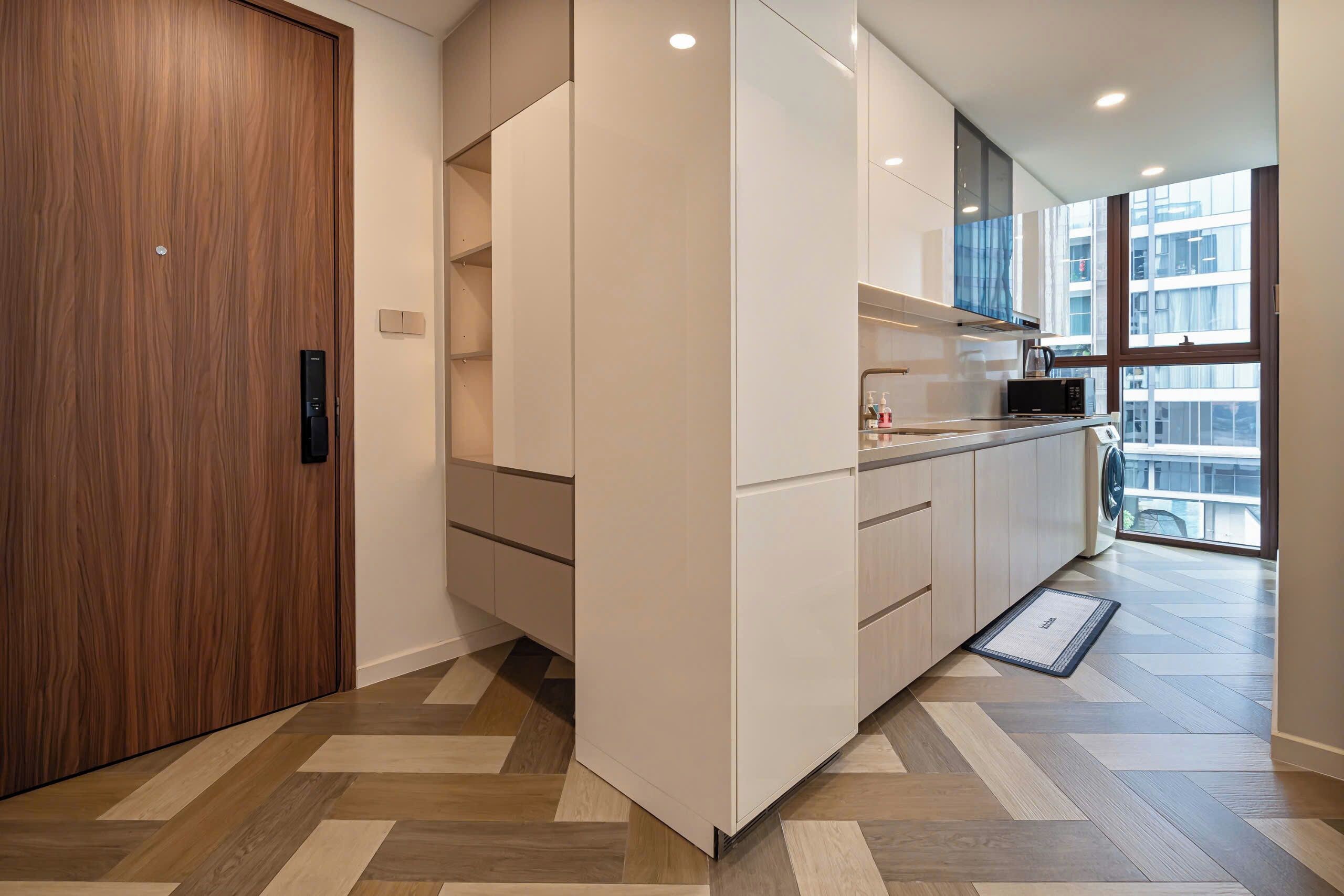 Una cocina moderna con armarios blancos, una puerta de madera y un piso con diseño en espiga.