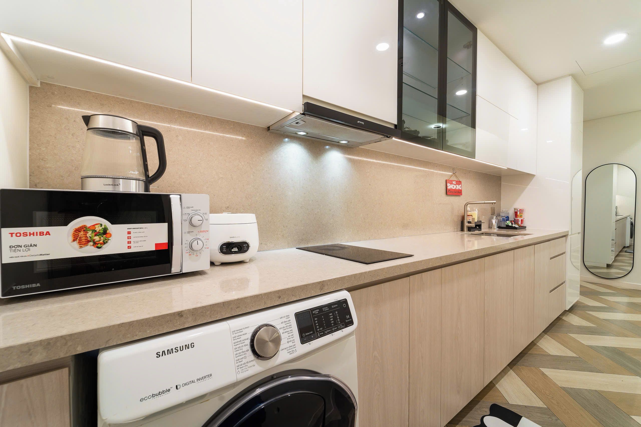 Uma cozinha moderna com um micro-ondas Toshiba, uma máquina de lavar louça Samsung e uma chaleira.