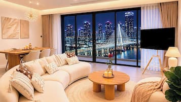 Una sala de estar moderna con un sofá grande, una mesa de centro redonda y vistas a la ciudad a través de amplias ventanas.