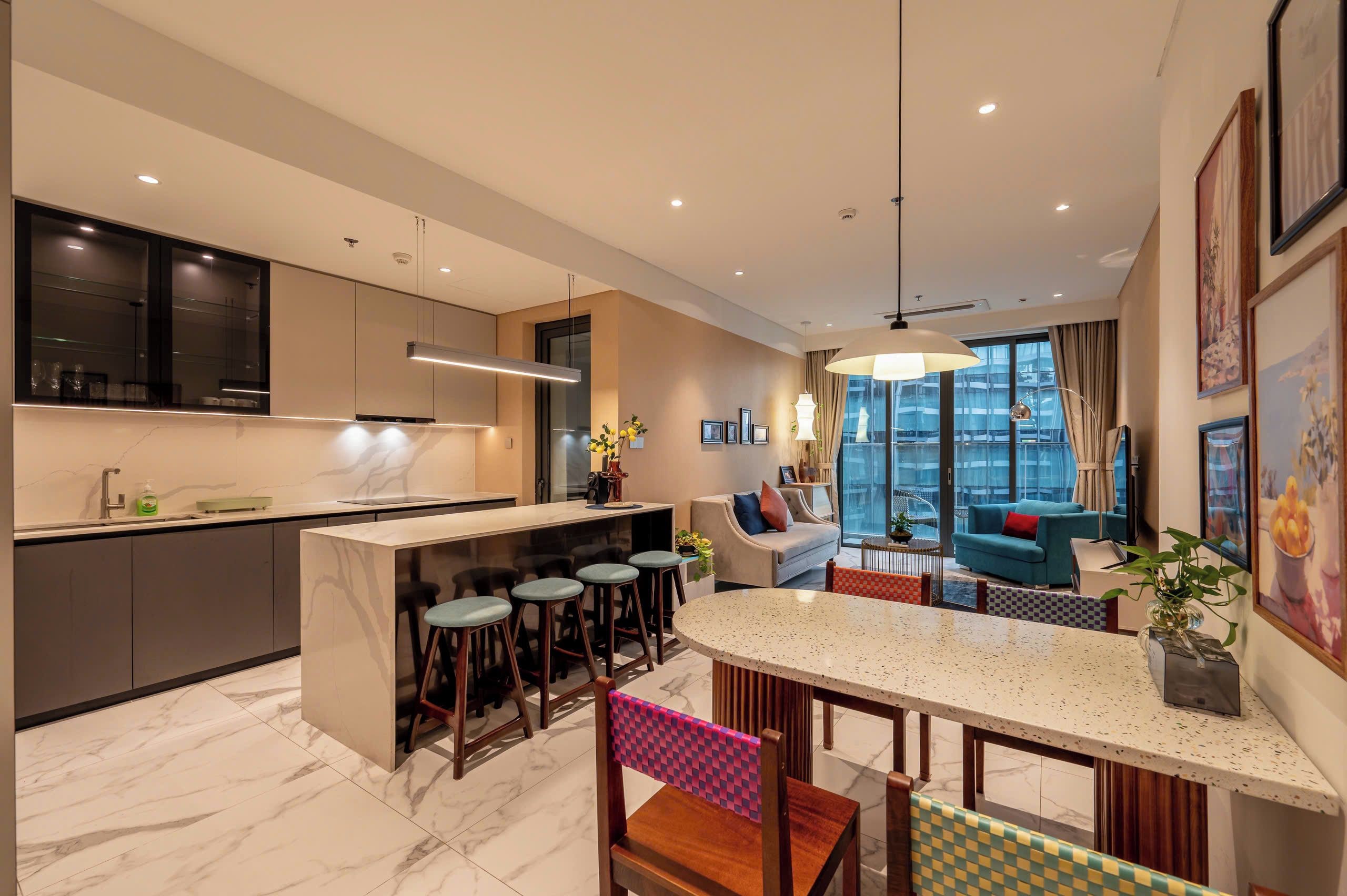 A modern kitchen with a central island, bar stools, and a dining area with a checkered chair.