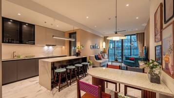 A modern kitchen with a central island, bar stools, and a dining area with a checkered chair.