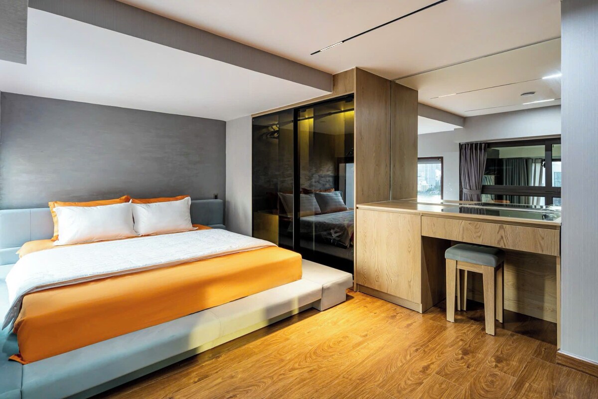 A modern bedroom with a bed, a desk, and a mirror.