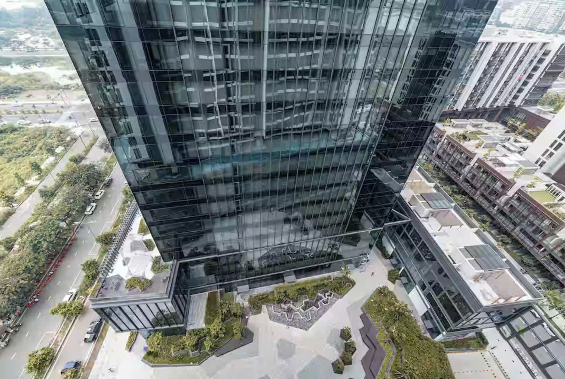 A modern high-rise building with a glass facade, surrounded by smaller structures and greenery.
