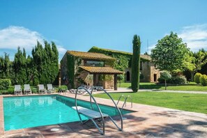 A swimming pool with lounge chairs and a stone building with a tiled roof.