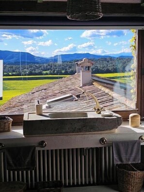 A bathroom with a large window overlooking a scenic landscape, a stone sink, and a towel rack. - Historic Catalan farmhouse with pool near Girona (Cornellà del Terri)