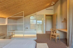A bedroom with a sloped ceiling, a bed, a chair, and a built-in wardrobe.