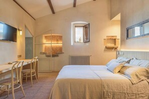 Ein Schlafzimmer mit einem Bett, einem Schreibtisch und Stühlen. Es gibt ein Fenster und eine Heizung.