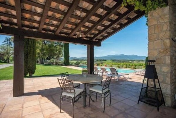 An outdoor patio with a pergola, a table with chairs, and a view of a swimming pool and mountains.
