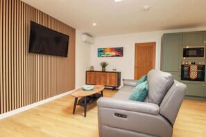 Ein modernes Wohnzimmer mit einer Ledersofa, einem kleinen Esstisch und einer Küchenzeile, inklusive Mikrowelle und Backofen.