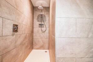 Eine schmale Duschkabine mit Handbrause und am Wand befestigtem Wasserhahn.