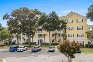 A multi-story residential building with balconies and a parking lot with several cars. - 10% off 3-7 nights thru Dec. 3rd flr. Elev. Pool view. Short walk to beach. (North Myrtle Beach)
