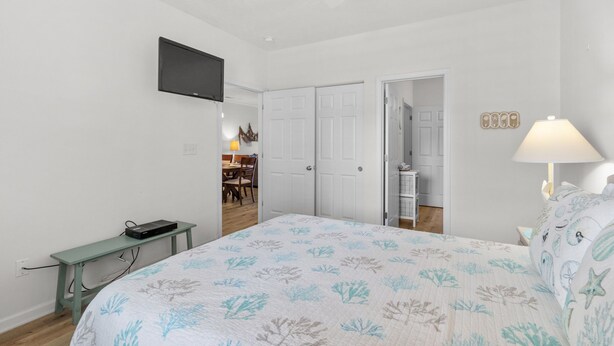 A bedroom with a bed, a TV mounted on the wall, a desk with a computer, and a door leading to a bathroom. - 10% off 3-7 nights thru Oct. 2BR 2BA condo. 3rd flr. Elev. Pool view. Short walk to beach. (North Myrtle Beach)