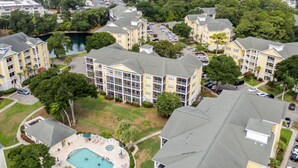 A residential area with multi-story buildings, a swimming pool, and a small lake. - 10% off 3-7 nights thru Oct. 2BR 2BA condo. 3rd flr. Elev. Pool view. Short walk to beach. (North Myrtle Beach)
