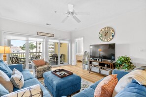 Ein Wohnzimmer mit einem blauen Sofa, einem Fernseher, einer Uhr und einem Deckenventilator.