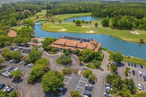 Vista aérea de um campo de golfe com um clube, estacionamento e um lago.