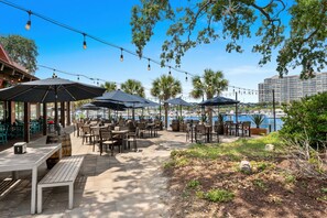 Un área de comedor al aire libre con mesas y sombrillas, con vistas a un puerto deportivo con barcos.