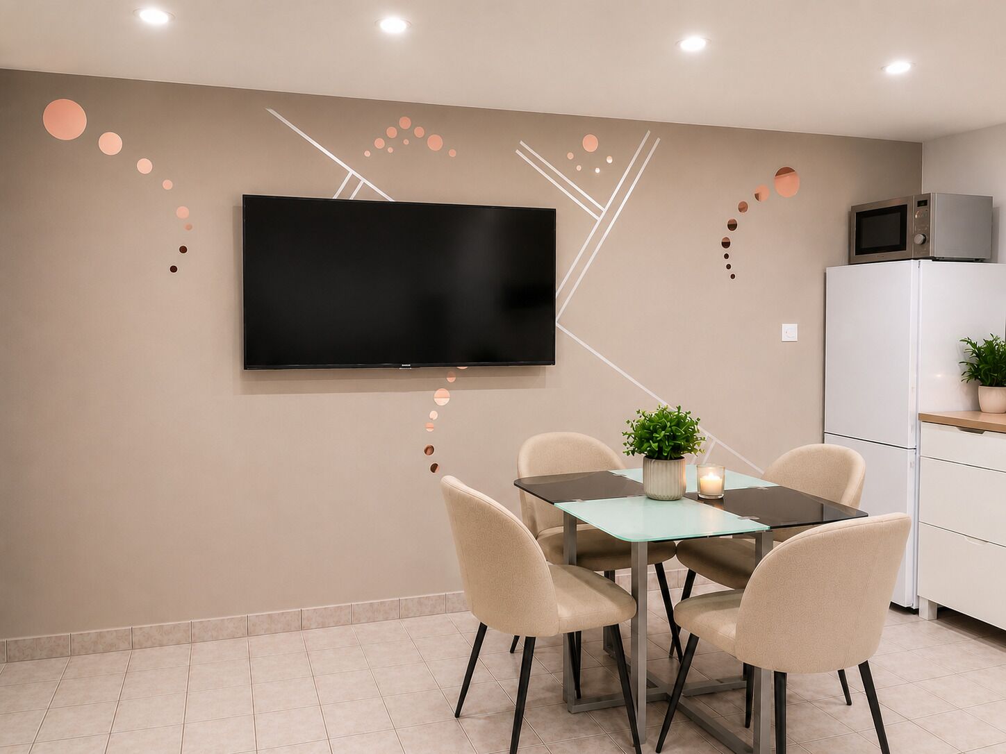 Ein moderner Essbereich mit einem an der Wand befestigten Flachbildfernseher, einem Tisch mit Stühlen und einem Kühlschrank im Hintergrund.