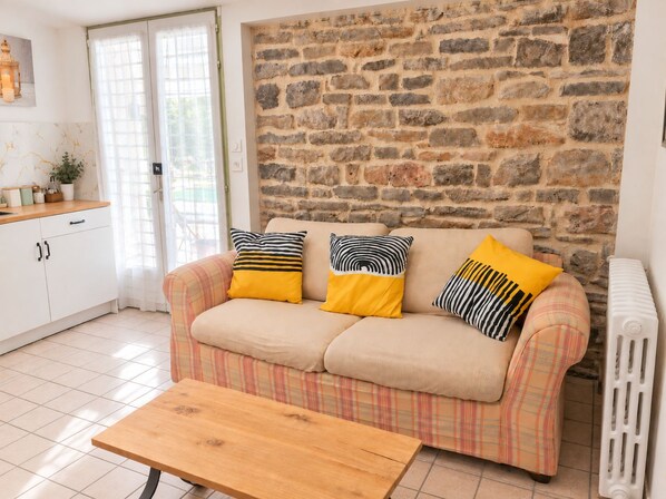 A living room with a stone wall, a sofa with plaid cushions, a wooden coffee table, and a radiator.
