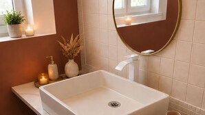 Un bagno con un lavandino bianco, uno specchio con cornice dorata e una finestra sopra il lavandino.