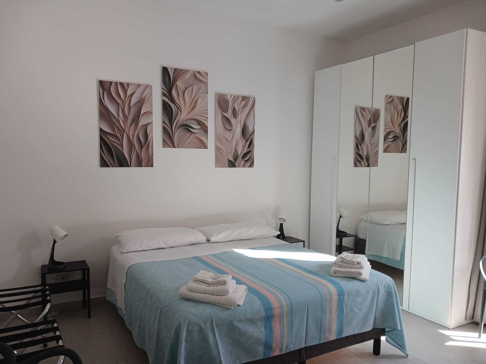 A bedroom with a bed, a nightstand, a lamp, a mirror, and artwork on the wall.