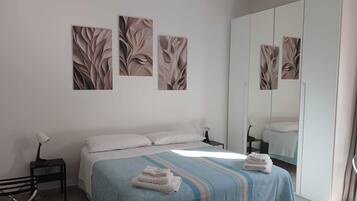 A bedroom with a bed, a nightstand, a lamp, a mirror, and artwork on the wall.