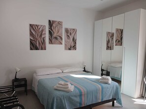 A bedroom with a bed, a nightstand, a lamp, a mirror, and artwork on the wall.
