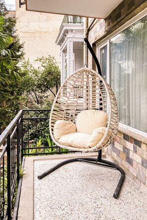 Ein Korbstuhl mit Kissen auf einem Balkon mit Fliesenboden.