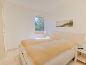 Ein Schlafzimmer mit einem Bett, einem Nachttisch, einer Lampe, einem Fenster und einem Bild an der Wand.