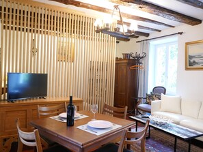 Ein Essbereich mit Holztisch, Stühlen, einem Fernseher und einer Weinflasche.