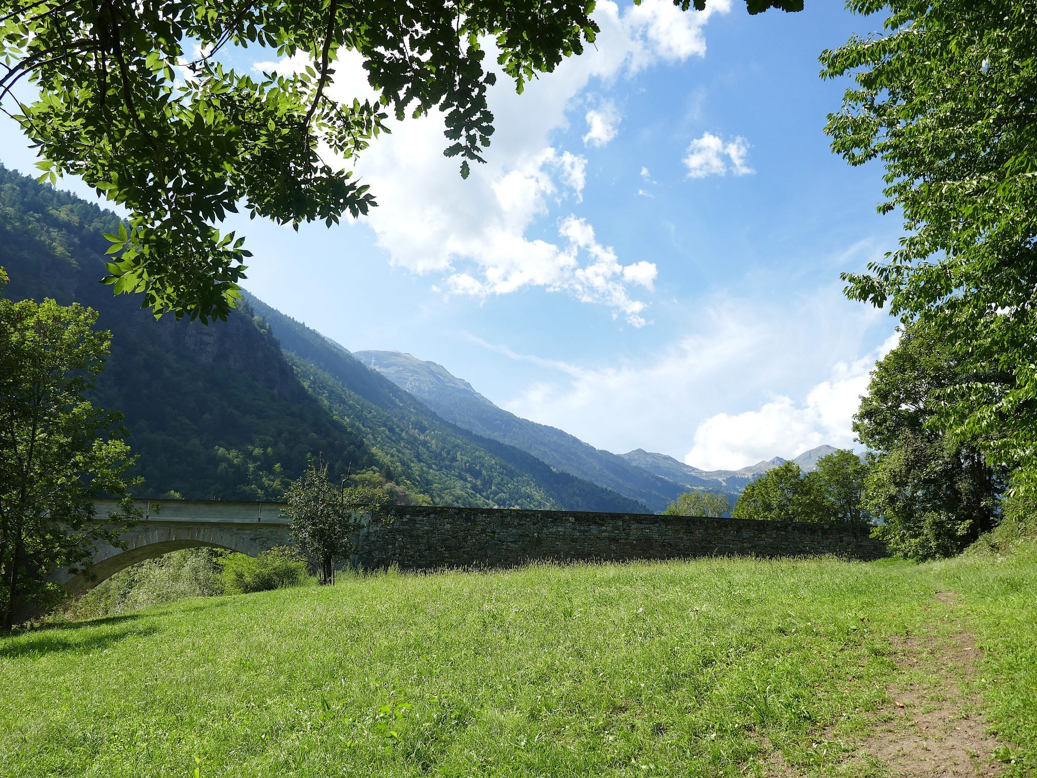 A stone bridge over a river, surrounded by lush greenery and mountains in the background.