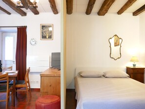 Ein Zimmer mit einem Bett, einem Schreibtisch mit Computer, einem Stuhl und einem Fenster mit Vorhängen.