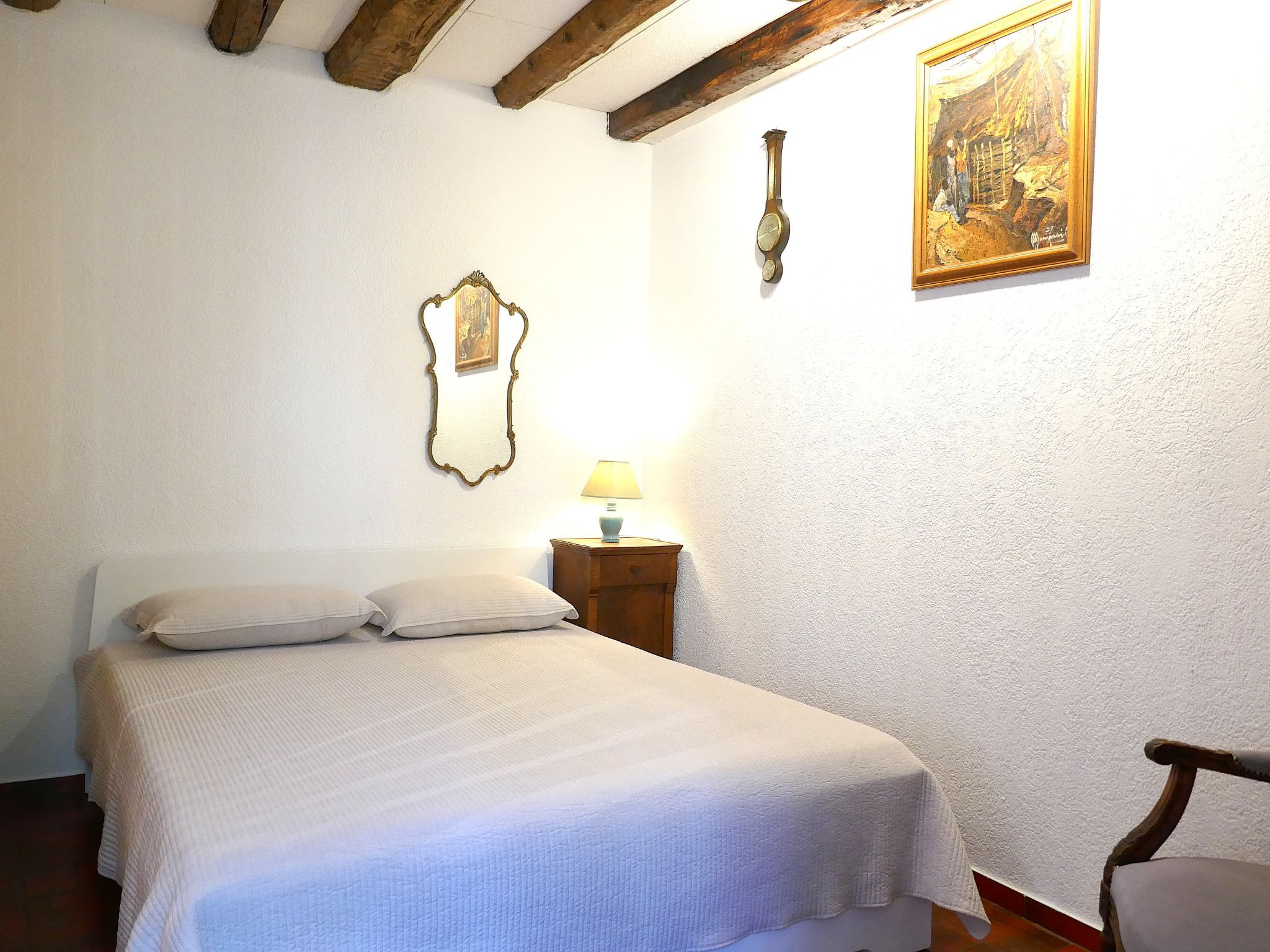 A bedroom with a bed, a nightstand, a lamp, a wall clock, and a framed picture.