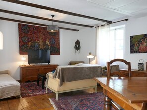 A cozy room with a bed, a desk, a television, and a dining table. There are two lamps, a rug, and a painting on the wall. - Apartment Dolfo by Interhome (Ludiano)