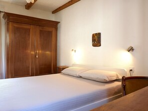 A bedroom with a large wooden wardrobe, a bed with white bedding, and a small bedside table. - Apartment Dolfo by Interhome (Ludiano)