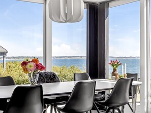Ein Essbereich mit Tisch und Stühlen, einer Blumenvase und Blick auf das Meer.