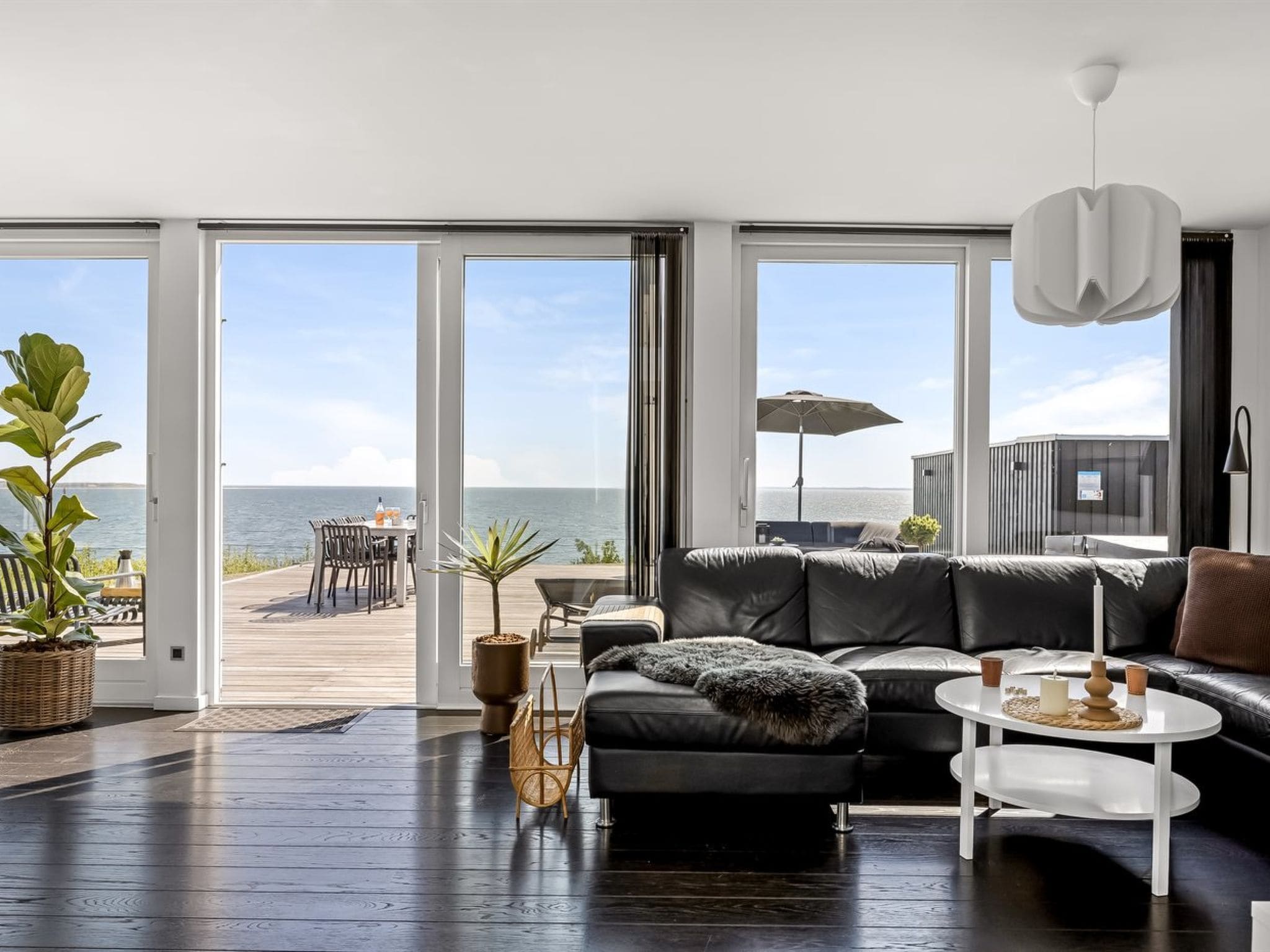 Una sala moderna con un sofá de cuero negro, una mesa de centro blanca y vista al mar a través de amplios ventanales.