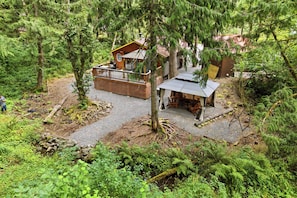 A cabin with a deck, surrounded by dense forest. - Perch - Whispering Pines | Romantic Rainier Cabin + Hot Tub (Ashford)