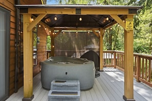 A hot tub under a wooden pergola with a caution sign for slippery surfaces. - Perch - Whispering Pines | Romantic Rainier Cabin + Hot Tub (Ashford)