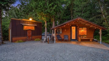 A cabin with a covered outdoor seating area and a separate building with a grill.